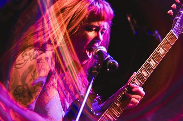 A musician singing and playing her guitar live on stage