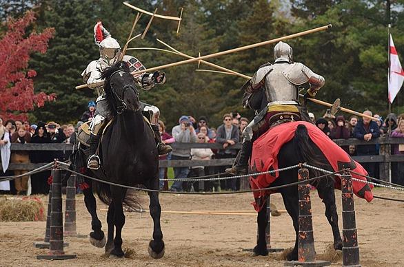 Two knights dressed in armour and riding horses are jousting outdoors at the Oxford Renaissance Festival