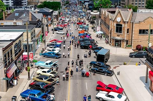 Classic cars on display on a street with a large group of people viewing them, located on Richmond Row in London, Ontario
