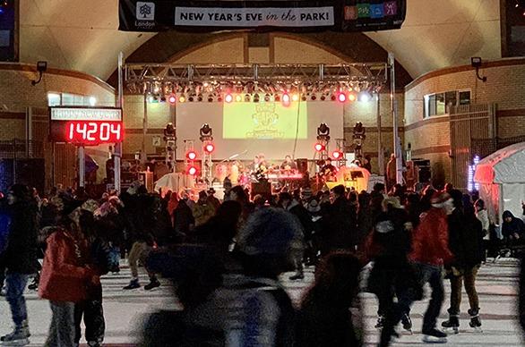 A large group of people skating outdoors at Victoria Park while a band plays live music on stage on New Years Eve in London, Ontario