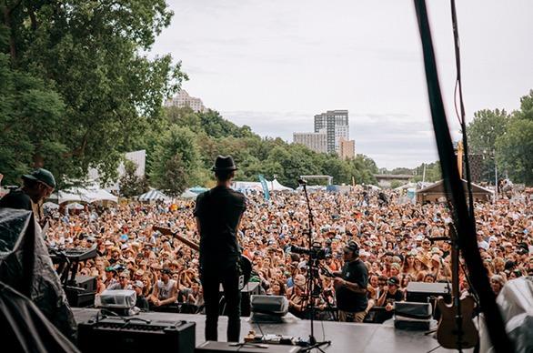 A musician playing live on stage looking out to a large crowd gathered outdoors at Rock the Park Festival in Harris Park located in London, Ontario