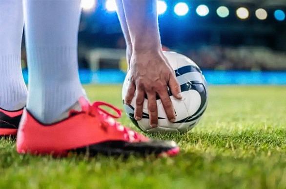 A soccer player placing a ball on the grass in a large stadium