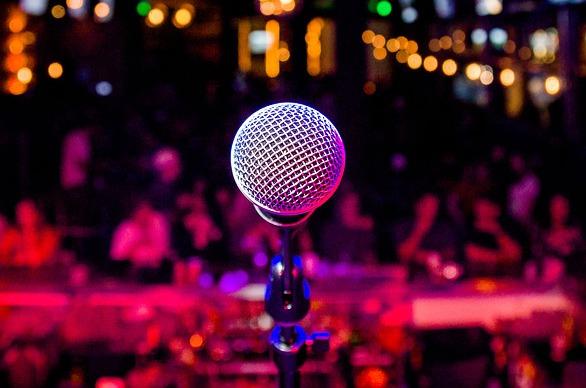A lone microphone on stage with an out of focus crowd in the distance.