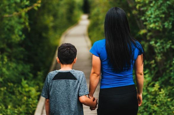 A mother and her son are walking on a wooden path surrounded by trees in Westminster Ponds located in London, Ontario