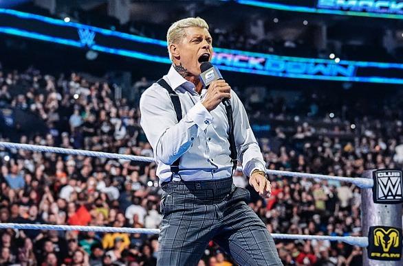 WWE Wrestler Cody Rhodes speaking into a microphone live on stage with a large crowd of people in the background