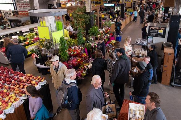 A crowd of people indoors at The Market at Western Fair District with various vendors selling fresh produce and various products