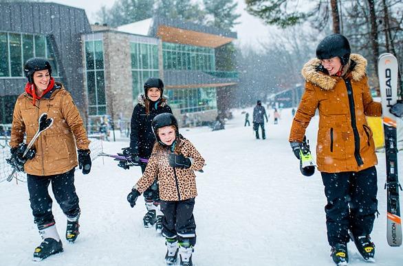 A family outdoors with skis on a snowy winter day, walking towards a ski hill at Boler Mountain located in London, Ontario