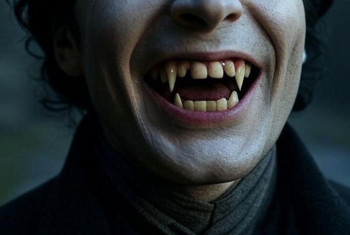 A close-up of a grinning vampire with sharp fangs, cut off at the eyes, wearing a dark coat.