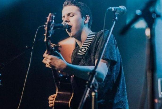 Ben Heffernan playing music onstage, singing with his guitar.