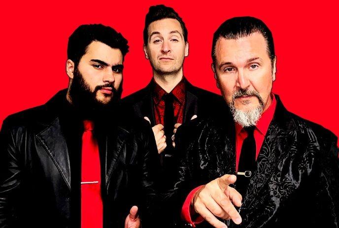 The 3 band members of Big Sugar posing for the camera, wearing black and red attire in front of a red background.