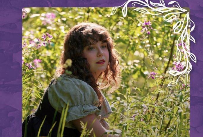 Woman with curly hair sits in a lush green field surrounded by wildflowers.
