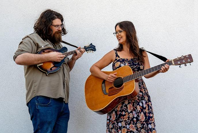 Allison Brown & Dan Henshall playing mandolin and guitar against white wall creating casual duet moment together.