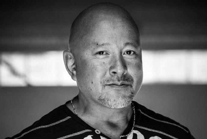 Artistic black-and-white photo of man with necklace, posing for a picture.