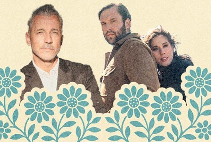 Three people stand behind blue floral border, one in suit, two in casual wear against plain beige backdrop.