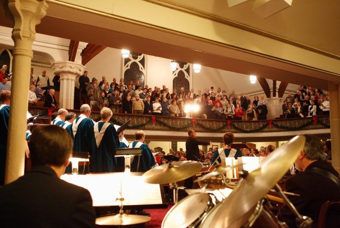 Choir and orchestra performing in a packed church sanctuary before a large audience.