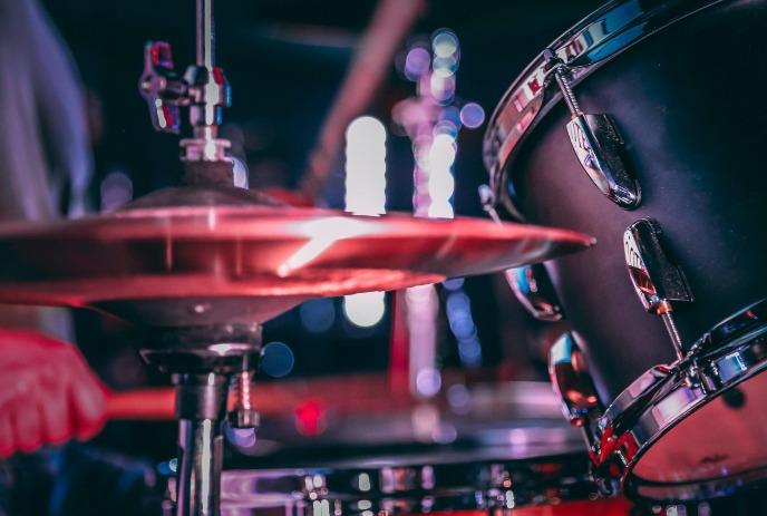 A close-up of a drum set with a hand striking a cymbal, illuminated by colorful stage lights.