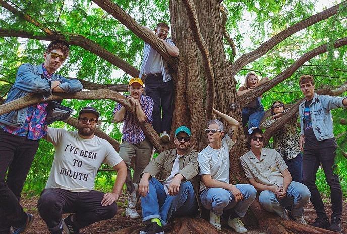 The 10 members of Dwayne Gretzky posing around a large tree on a sunny day.