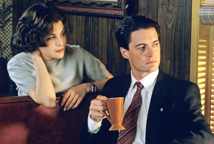 Two people sit in warm wood booth as one holds mug and looks aside in quiet retro diner scene.