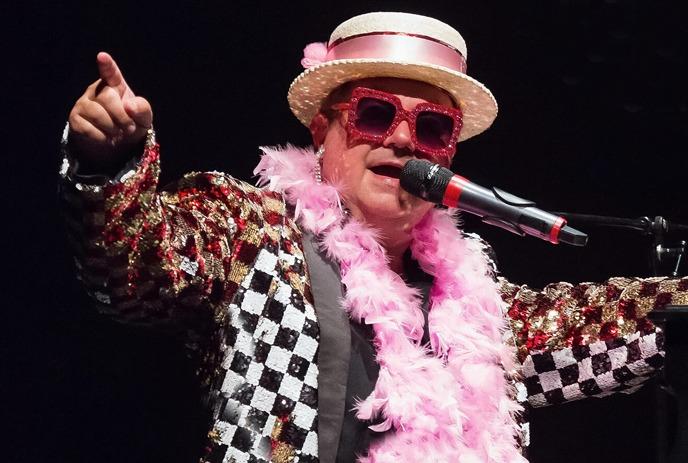 Jeff Scott performing on a piano on stage, dressed as Elton John