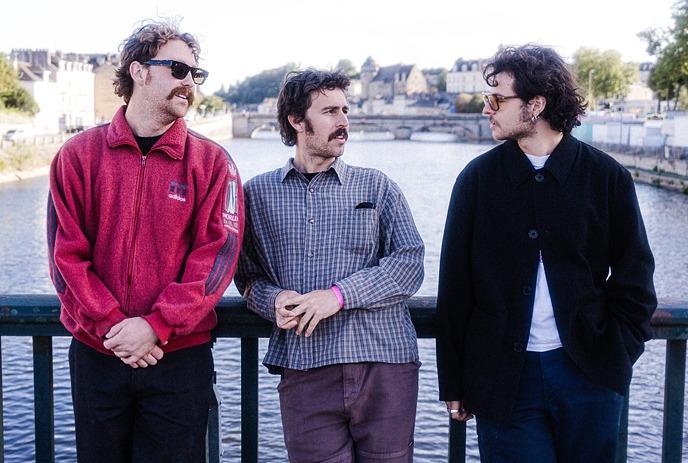 Three members of the band The Grogans standing on a bridge overlooking a river.
