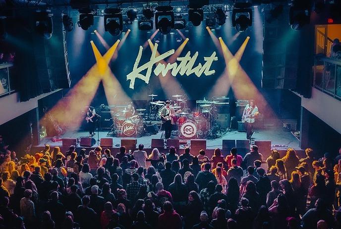 Hartlet performing on stage in front of a crowd, with their band name on the stage screen.