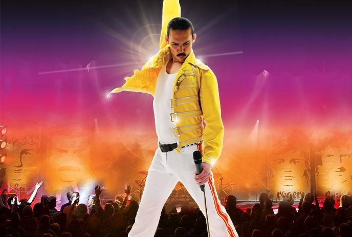 Dynamic stage scene with a performer in a yellow jacket and white outfit, arm raised triumphantly.