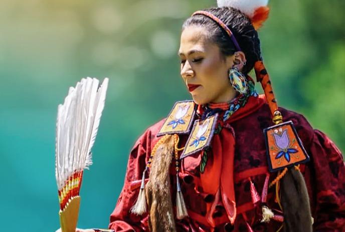 An Indigenous person in ceremonial attire dancing with an eagle flying beside them.