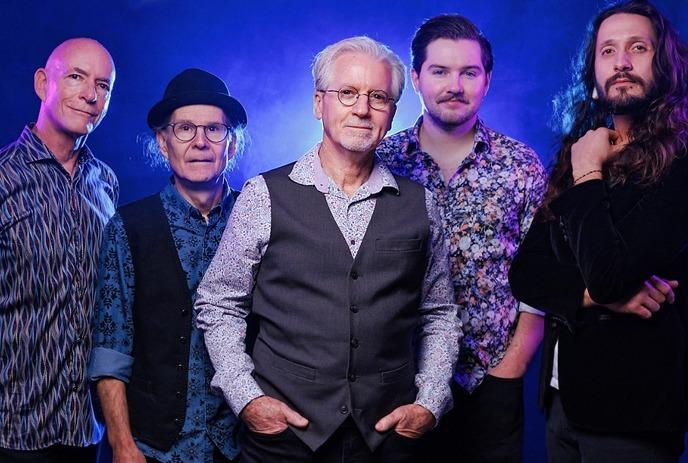 5 musicians from The Doobie Brothers tribute band pose together in a line, behind a blue wall with smoke in the air.