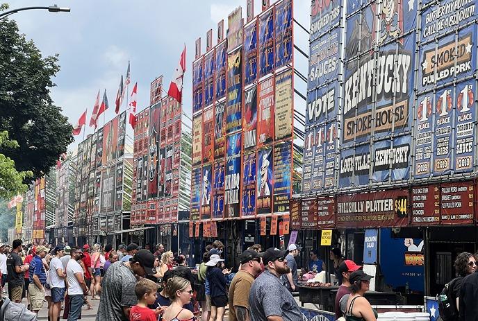 Ribfest with food stalls, colorful banners, grilling meat, and crowds enjoying the event.