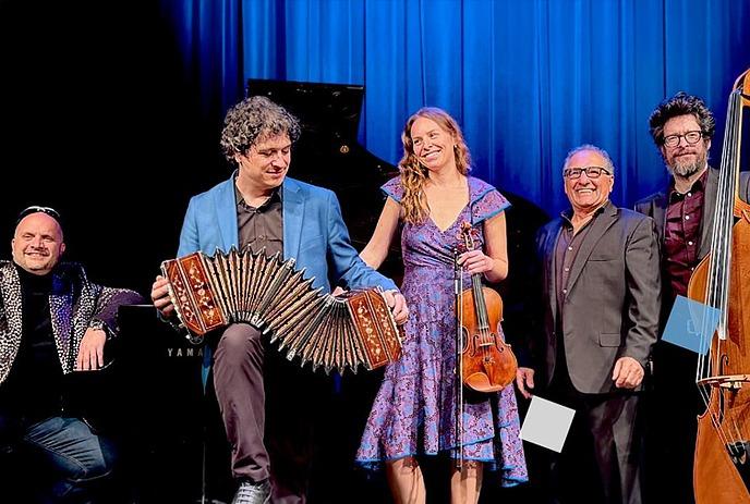 Musicians on stage with piano, bandoneon, violin, and bass, dressed formally, ready for a concert.