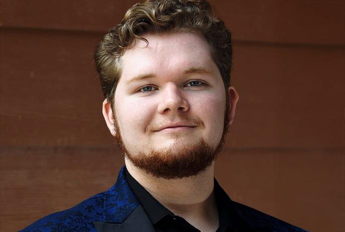 Artist in blue patterned blazer and shirt smiles gently against dark blue backdrop with soft abstract shapes.