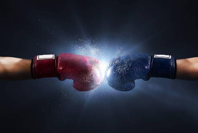 Red and blue boxing gloves hitting each other with a white spark in between them