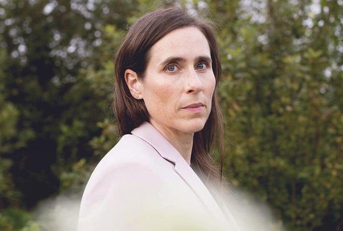 Rose Cousins in pale blazer stands in green foliage.