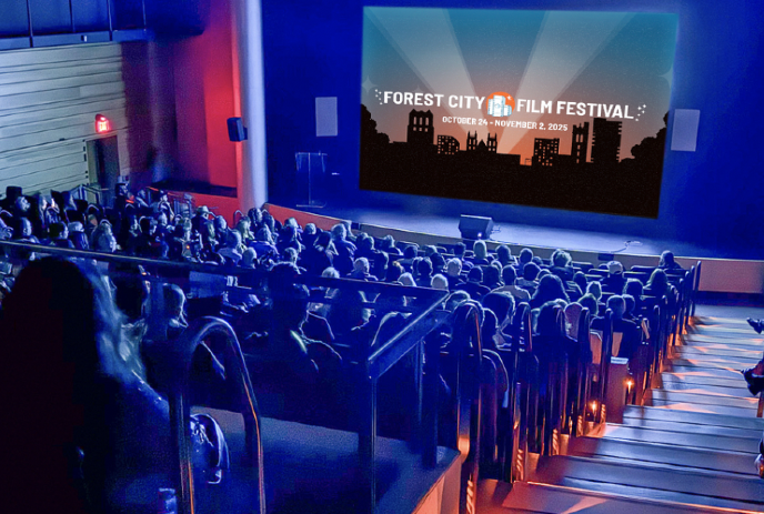 A crowded theater watches a screen displaying the Forest City Film Festival.