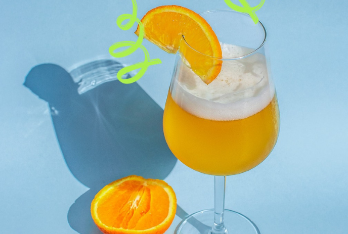 A refreshing orange cocktail with a slice of orange and a green curly straw, served in a glass on a light blue surface.