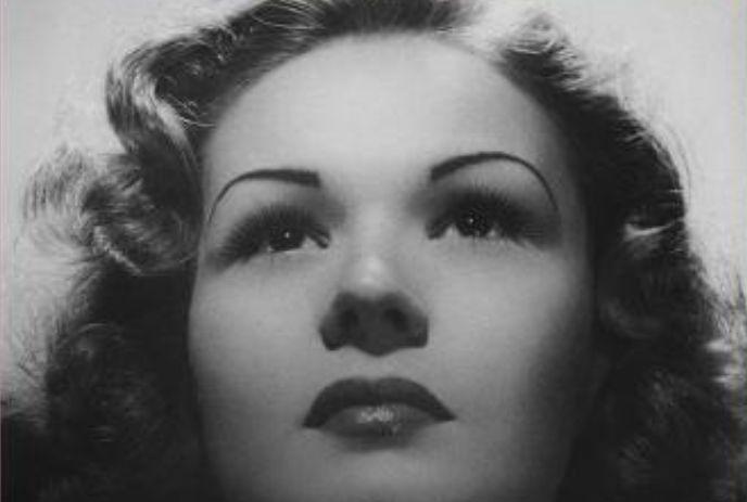 Vintage black-and-white portrait of person with wavy hair, dramatic lighting, and upward gaze.