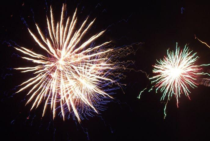 Bright twin fireworks burst across dark sky with vivid streaks of red, green yellow white light glow.