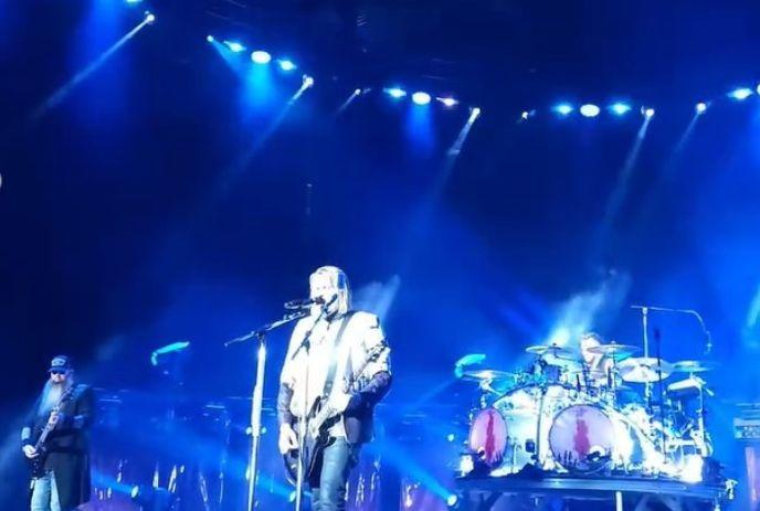 Bright stage lights frame band trio rocking guitars and drums in vivid blue haze creating energetic live vibe.