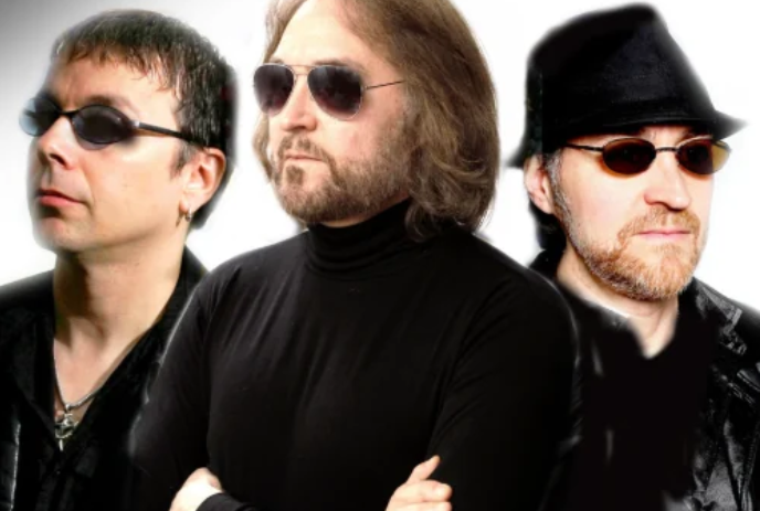 Three people wearing black clothes and black sunglasses stand together.