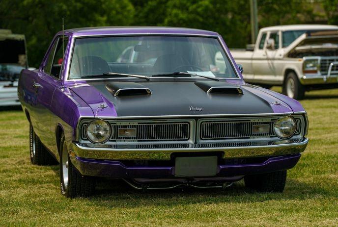 Purple Dodge muscle car parked on grass with black hood scoops at outdoor auto show.