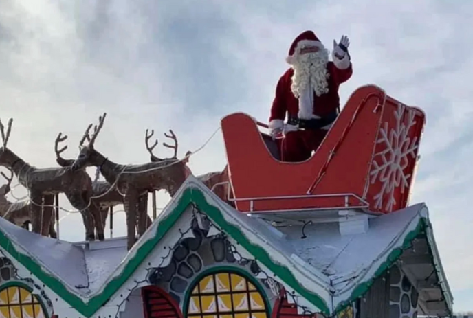 Santa on a sleigh being pulled by reindeer on top of a roof.