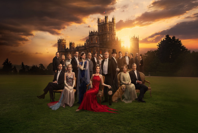 Group photo of all characters of Downton Abbey in front of the Abbey, under a cloudy sky.