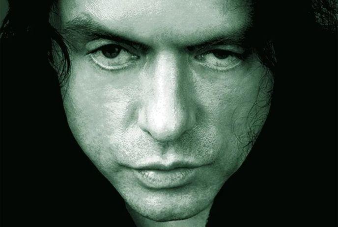 Close-up portrait of a person’s face with dark hair and intense gaze against a dark background.