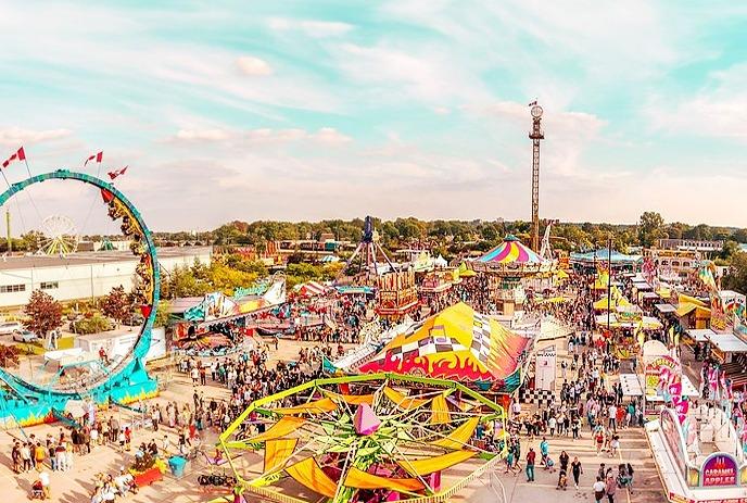 Carnival scene: vibrant rides, colorful tents, crowds enjoying festivities under a partly cloudy sky.