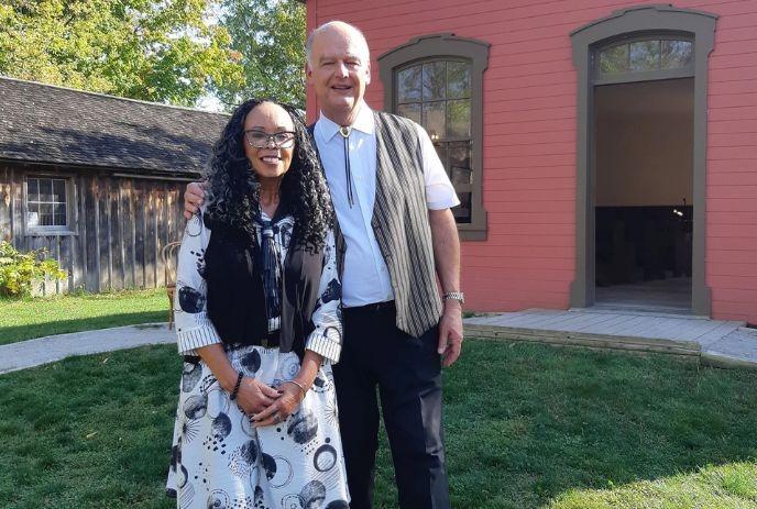 Denise Pelley next to a man, in front of the AME Church at Fanshawe Pioneer Village.