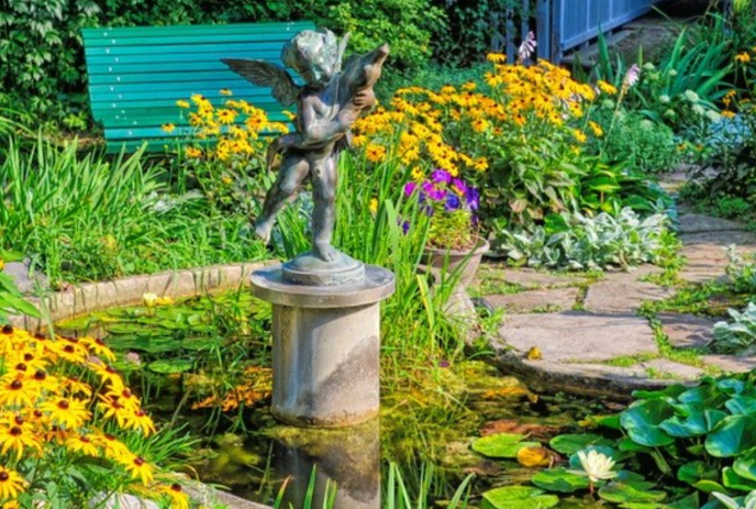 Cherub on a pedestal in the middle of a pond surrounded by gardens.