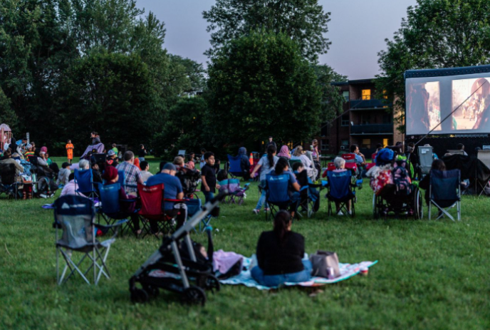 People sitting in lawn chairs in front of a large portable movie screen.