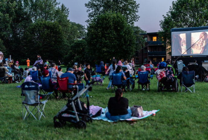 People sitting in lawn chairs in front of a large portable movie screen.
