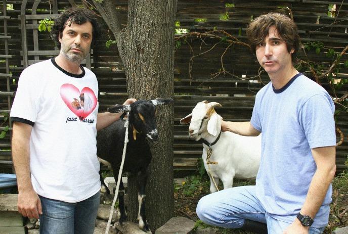 Kenny and Spenny, one with a black goat and one with a white goat, in an outside setting.