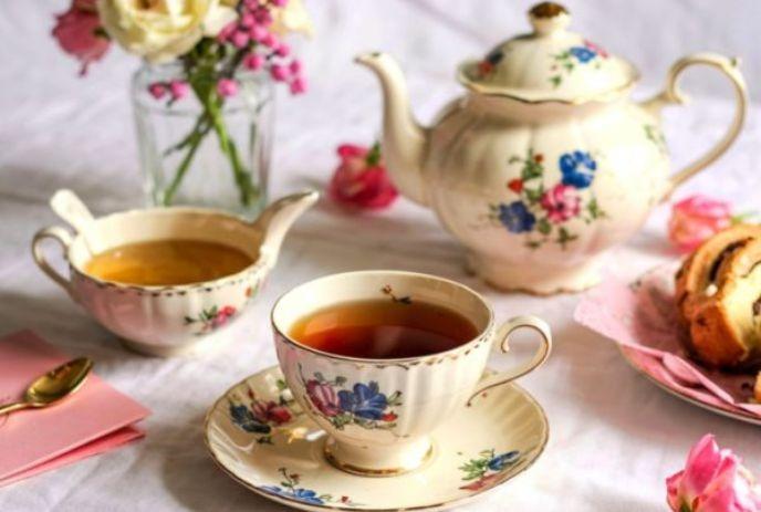 Floral tea set with cup teapot creamer pink napkin gold spoon pastries and fresh flowers on table